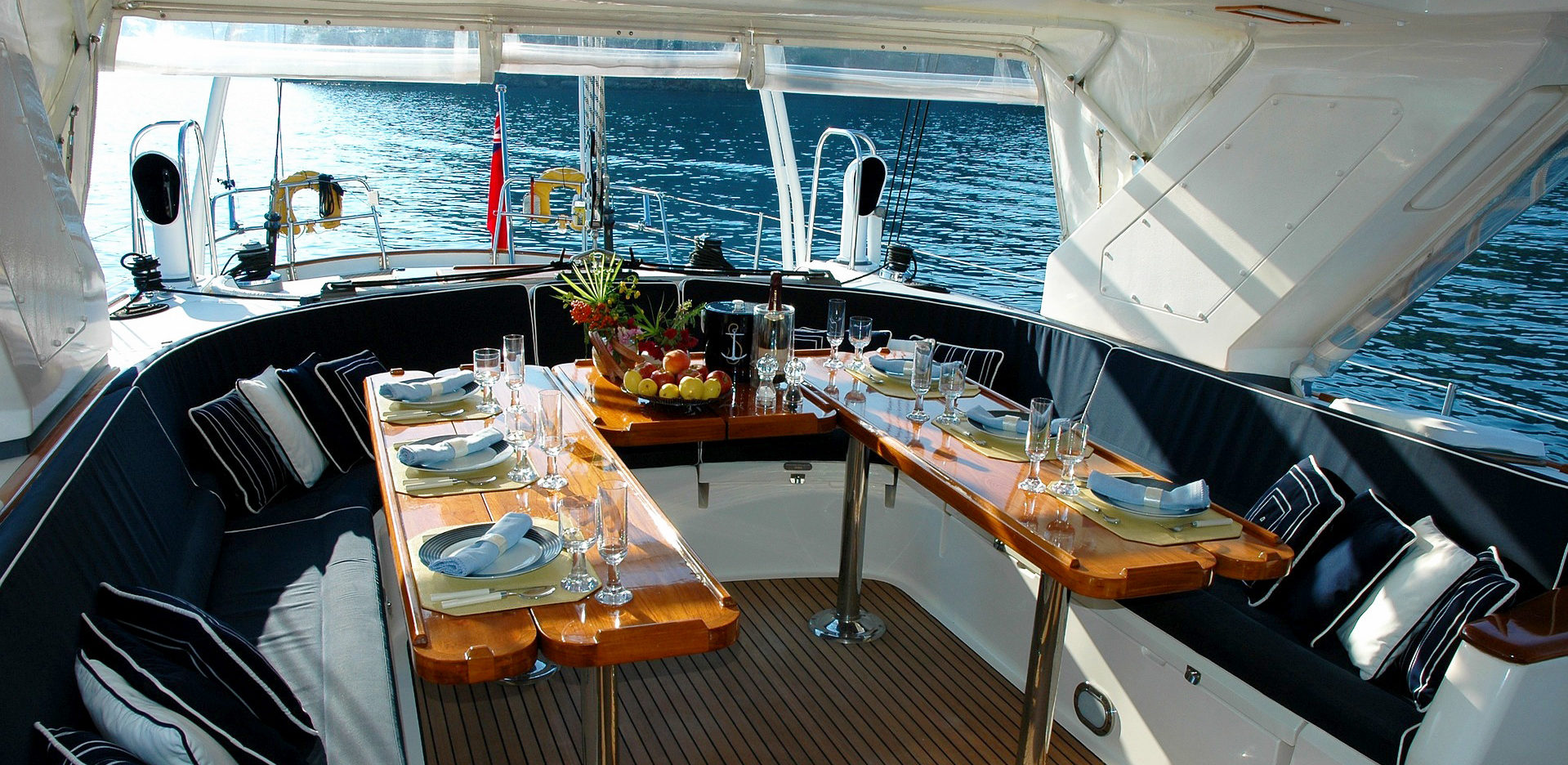 Ein eleganter, gedeckter Tisch auf dem Deck einer Yacht, bereit für ein luxuriöses Abendessen, mit Blick auf das Wasser im Hintergrund.