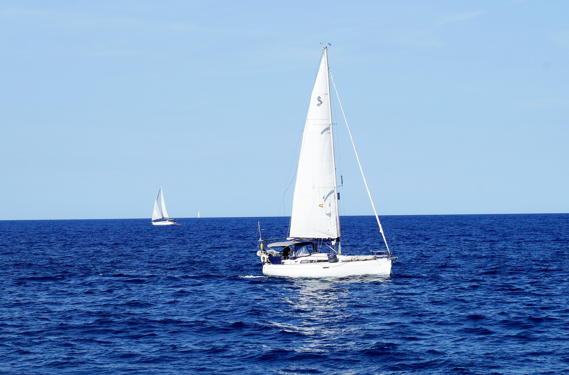 Ein Segelboot segelt auf dem offenen Meer bei klarem Himmel, im Hintergrund ist ein weiteres Segelboot zu sehen.