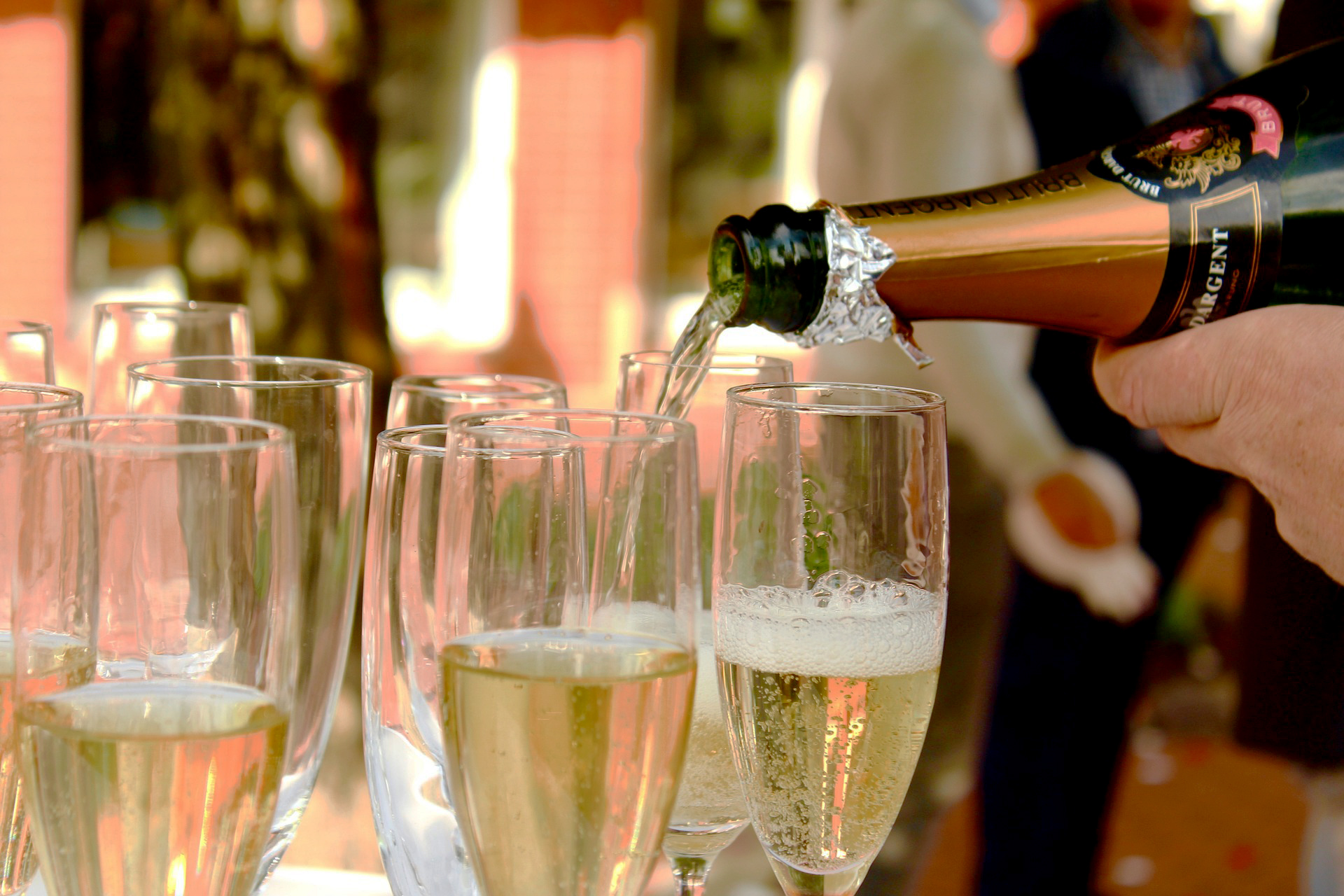 Nahaufnahme einer Hand, die Champagner in mehrere Gläser einschenkt, mit unscharfem Hintergrund.