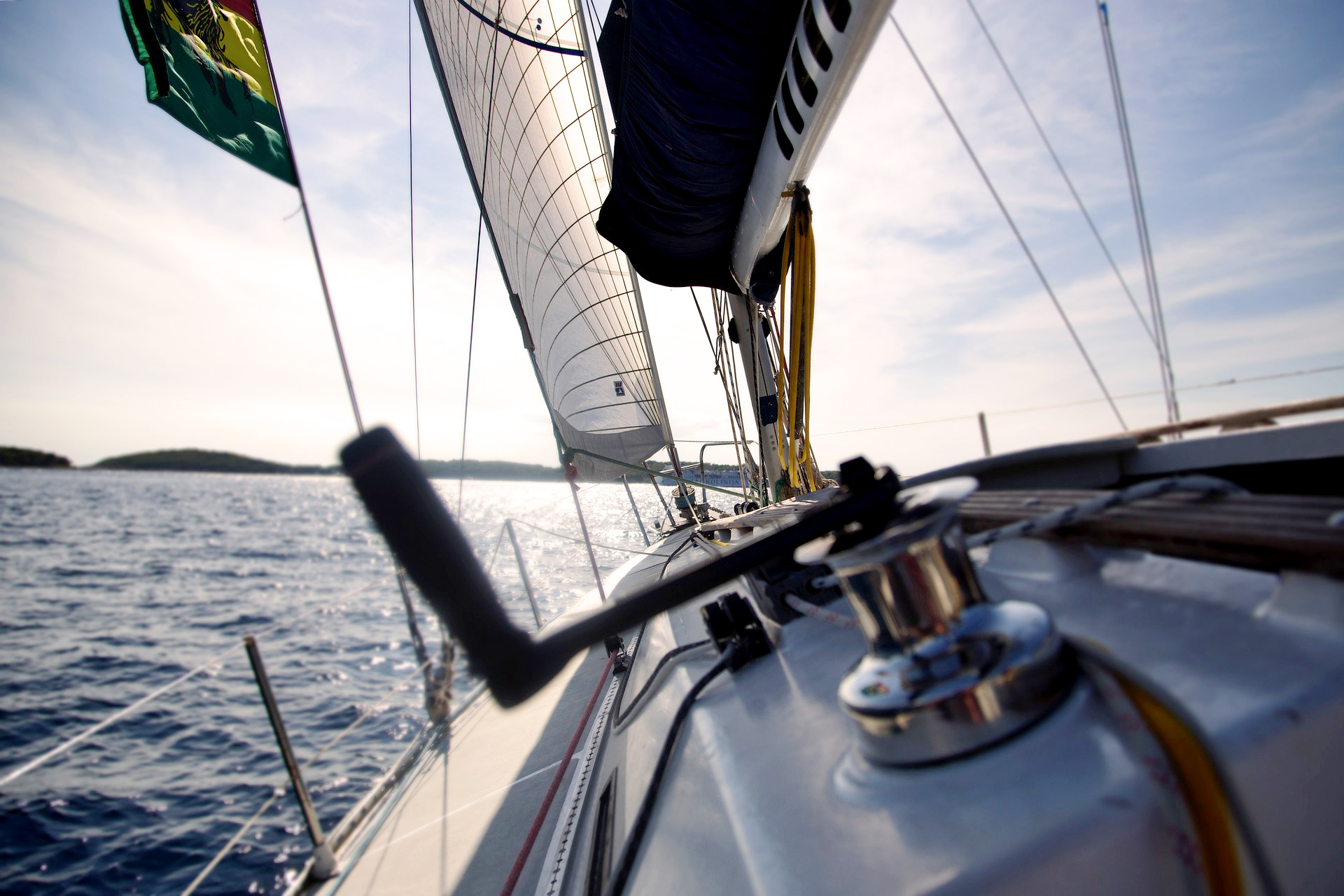 Blick vom Deck eines Segelbootes auf das Meer bei sonnigem Wetter, mit gespannten Segeln und einem klaren Himmel im Hintergrund.