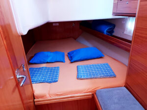 Eine Kabine auf einem Segelboot mit einem Doppelbett, ausgestattet mit orangefarbener Bettwäsche, blauen Kissen und Decken.